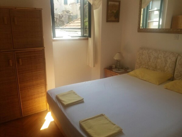 Un dormitorio con cama, mesita de noche, lámpara, ventana y armario.
