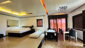 A modern hotel room with a large bed, a desk with chairs, a dining table, and a view of the outside through red curtains. - Tugsaw Resort (El Salvador)