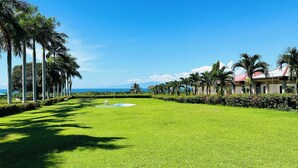 A well-maintained lawn with a small pond, palm trees, and a building with a red roof. - Tugsaw Resort (El Salvador)