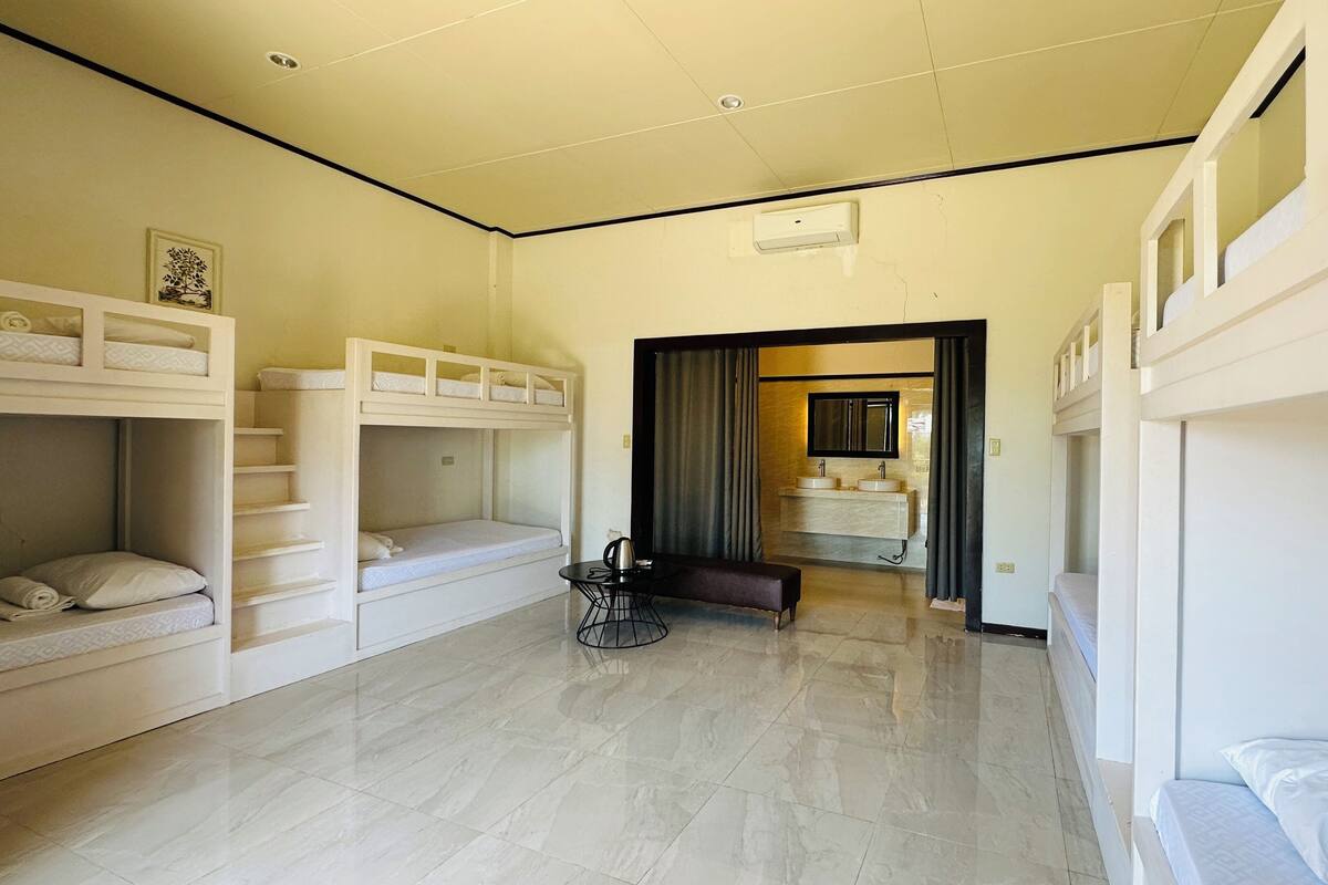 A dormitory room with bunk beds, a small seating area, and a bathroom visible through an open doorway.