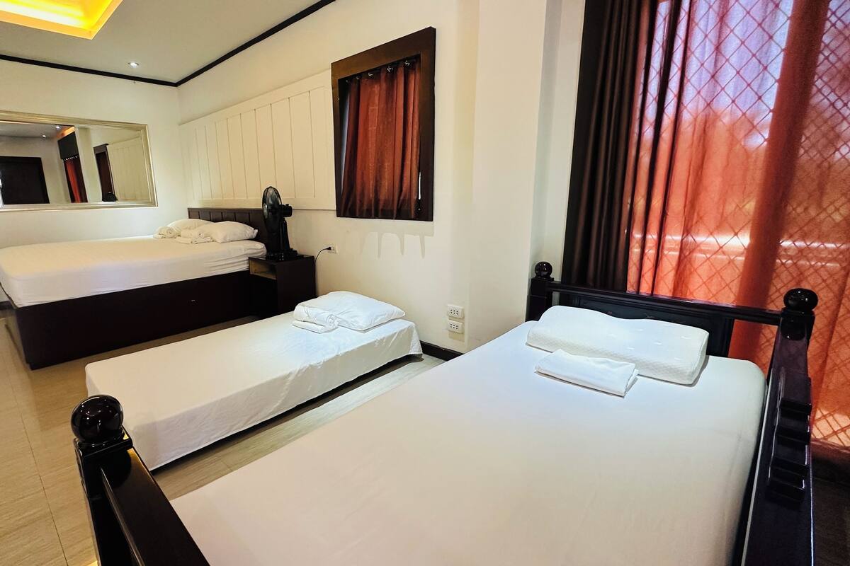 A hotel room with two single beds, a large mirror, a vanity with a mirror, and a window with red curtains.