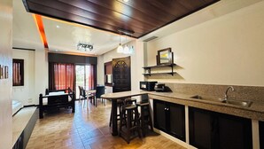 A modern kitchen with a central island, a dining area with a table and chairs, and a separate bedroom with a bed and window. - Tugsaw Resort (El Salvador)