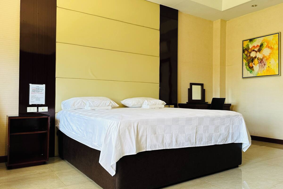 A hotel room with a bed, bedside table, and a painting on the wall.