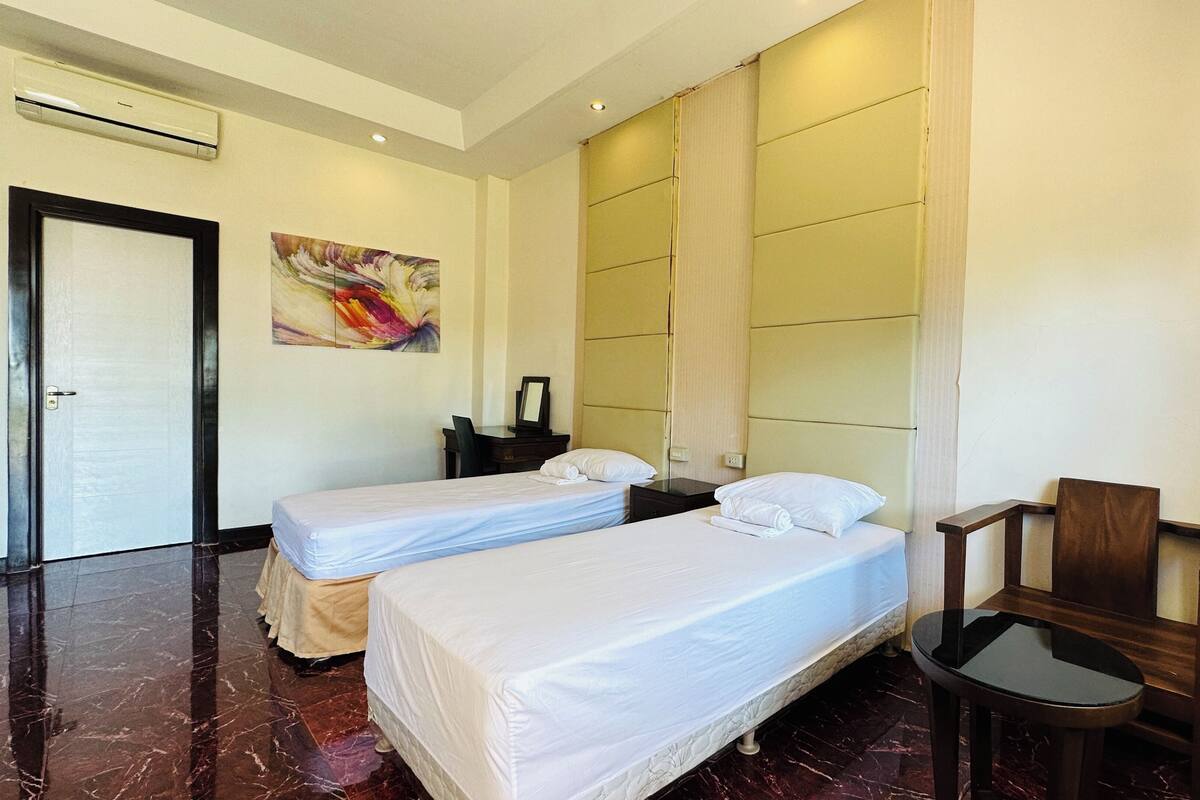A hotel room with two single beds, a desk, a chair, and a painting on the wall.