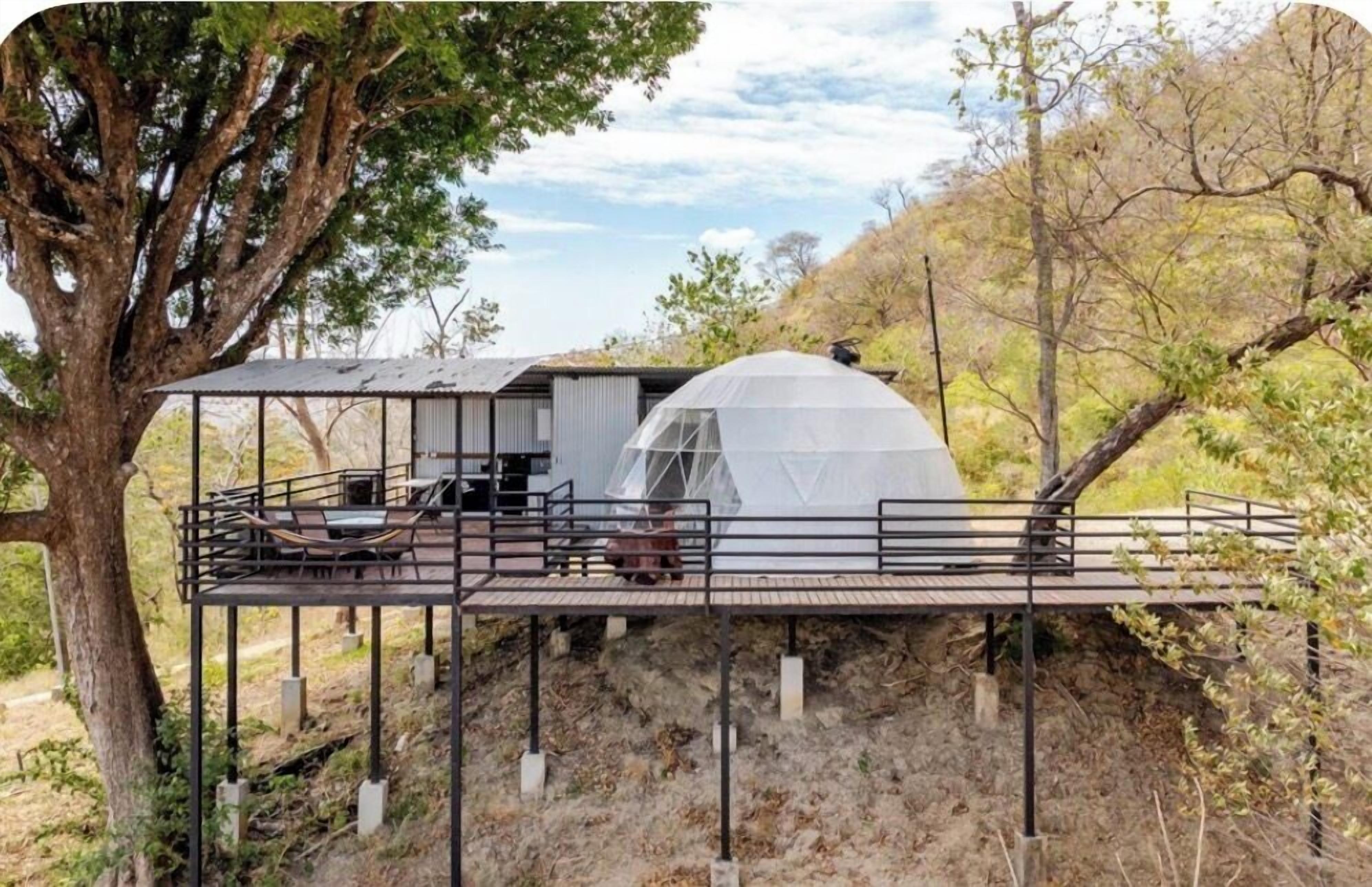 A dome-shaped structure with a wooden deck and metal railings, surrounded by trees and natural landscape.