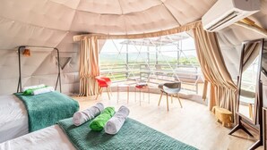 Ein Zelttyp-Zimmer mit Bett, grünen Handtüchern, einem kleinen Tisch, einem Stuhl und einem Fenster mit Vorhängen.