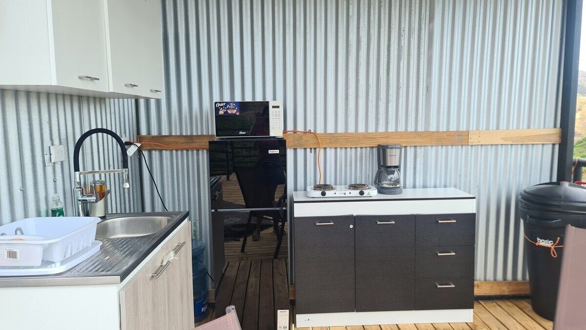 Een kleine keuken met een magnetron, fornuis, spoelbak en kastjes.