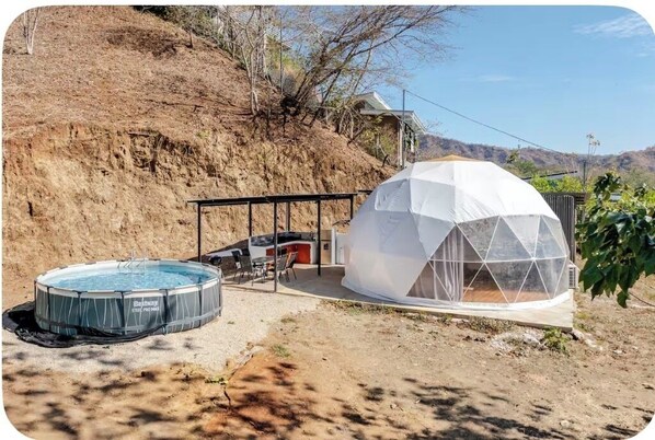 Uma estrutura em forma de cúpula geodésica com piscina e área de estar ao ar livre.