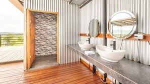 Ein modernes Badezimmer mit Holzboden, zwei Waschbecken, einem großen Spiegel und Blick ins Freie.