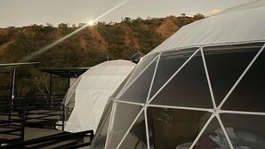 Eine Reihe von kuppelförmigen Zelten mit Metallgestell vor einer Hügellandschaft im Abendrot.
