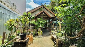 Ein traditionelles japanisches Gebäude mit einem Ziegeldach und Holzdecken, umgeben von üppiger Vegetation und Topfpflanzen.