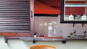 Eine Küche mit Fenster, ein Regal mit Küchenutensilien, ein Laptop und ein Korb voller Kiefernzapfen.