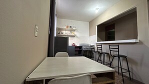 Een compacte keuken met een eethoek, met een houten tafel en stoelen, een koelkast en een fornuis.
