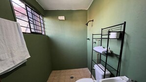 Een kleine badkamer met groene wanden, een toilet, wastafel en een metalen open kast.