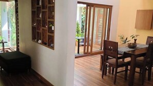 Un coin repas avec une table et des chaises en bois, un pouf noir et une porte-fenêtre coulissante donnant sur une terrasse extérieure.