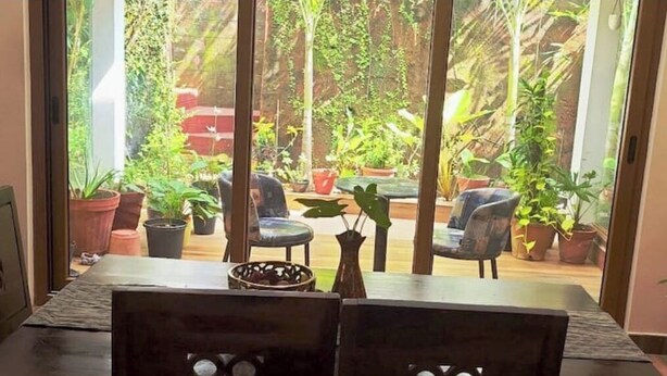 Une pièce dotée d’une grande porte-fenêtre coulissante donnant sur un jardin agrémenté de plantes en pot et de mobilier d’extérieur.