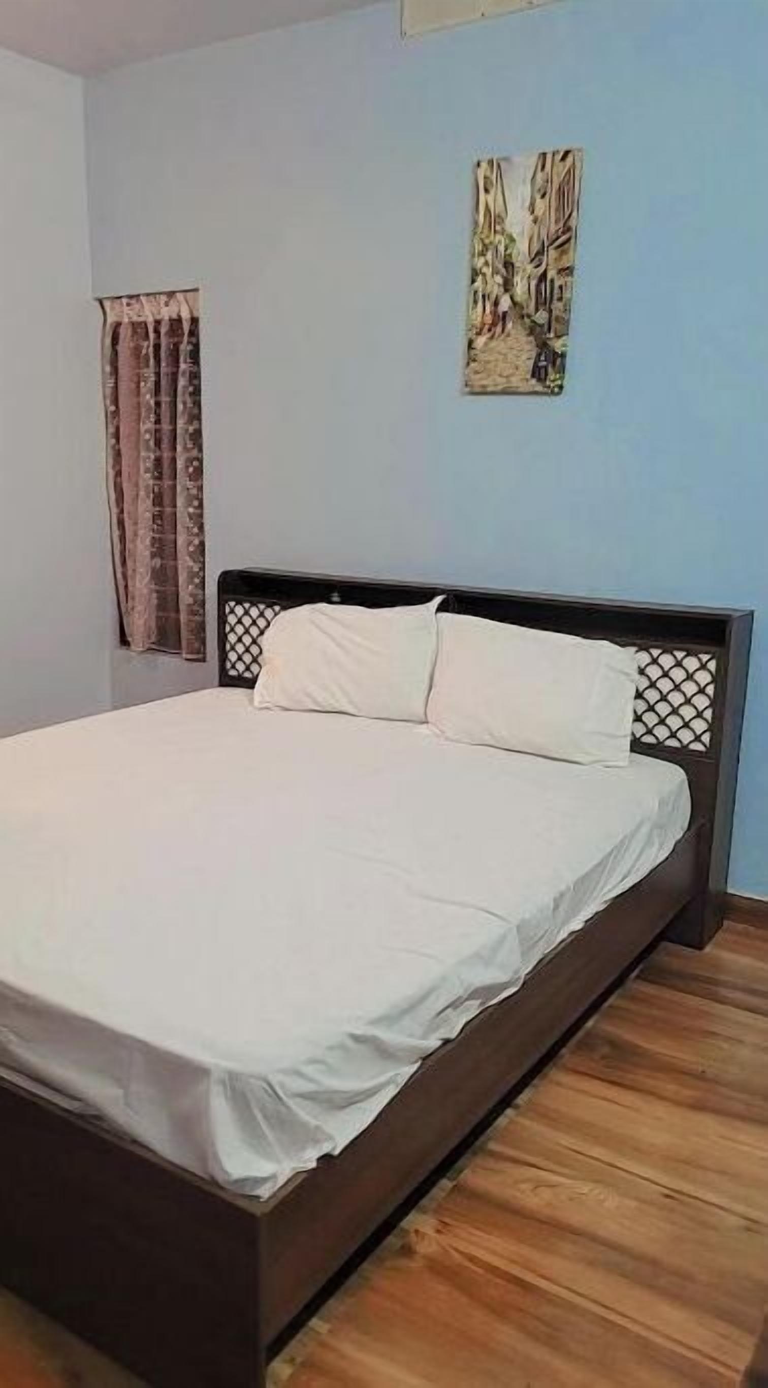 Une chambre avec un lit en bois, une fenêtre avec des rideaux et une œuvre d’art accrochée au mur.