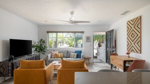 A modern living room with a flat-screen TV, two mustard-colored sofas, a wooden dining table, and a ceiling fan. - Leucadia "Ponto" Bungalow ~ walk everywhere with beach gear! (Encinitas)