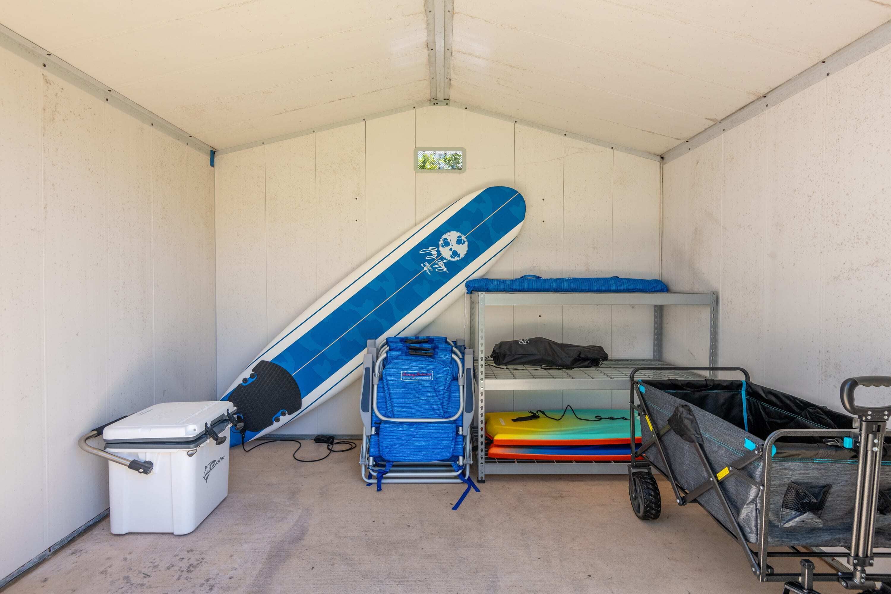 A storage room with a bunk bed, a blue surfboard, a cooler, and a cart with bags.