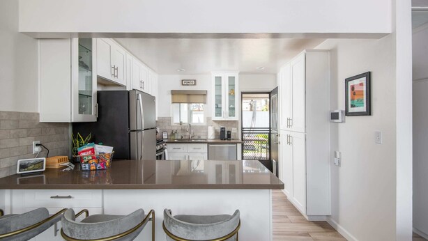 A modern kitchen with white cabinets, a central island with bar stools, and a refrigerator. - Leucadia "Ponto" Bungalow ~ walk everywhere with beach gear! (Encinitas)