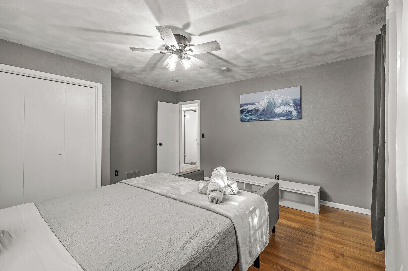 Un dormitorio con una cama, un ventilador de techo, un cuadro y una puerta que da a otra habitación.