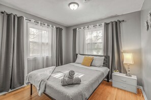 A bedroom with a bed, curtains, a bedside table with a lamp, and a window.