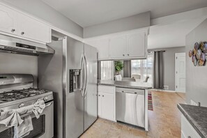 A modern kitchen with stainless steel appliances, white cabinetry, and a tiled floor.