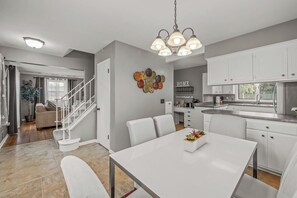 A modern kitchen with white cabinets, a dining area with a white table, and a staircase leading to a living area.