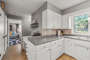 A modern kitchen with white cabinets, a granite countertop, and a window with a view of greenery.