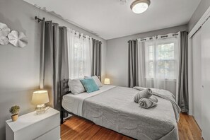 Een slaapkamer met een bed, nachtkastjes, een lamp en gordijnen.