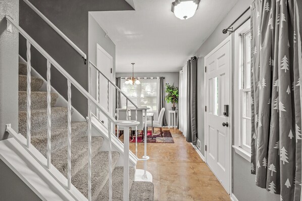 A hallway with a staircase, a dining area, and a door with curtains.