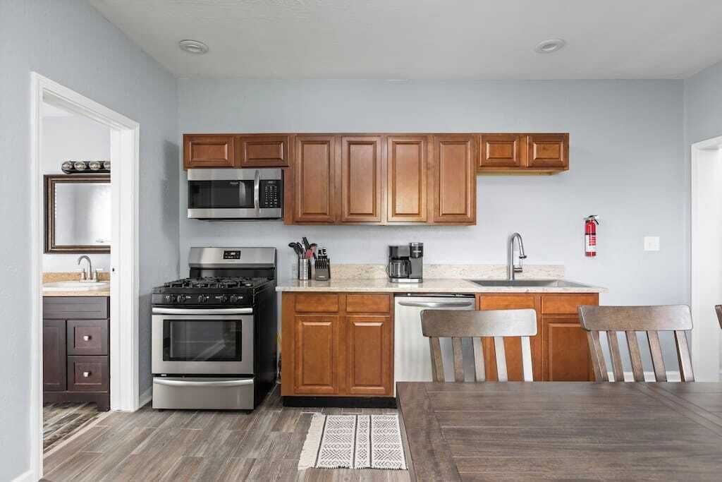 A compact kitchen with wooden cabinets, stainless steel appliances, and a dining area with a wooden table and chairs.