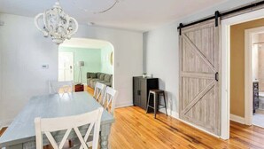 A dining area with a wooden table and chairs, a chandelier, and a sliding barn-style door. - The Germantown Gem | 4BR | Ideal Location | Patio (Louisville)