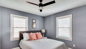 A bedroom with a bed, two windows with blinds, a ceiling fan, and a nightstand with a lamp. - The Germantown Gem | 4BR | Ideal Location | Patio (Louisville)