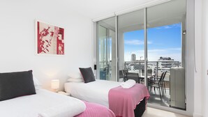 Une chambre d’hôtel avec deux lits, un balcon donnant sur la ville et une grande fenêtre.