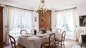 Un coin repas avec une table dressée pour quatre personnes, entourée de chaises, d’un lustre et de rideaux.