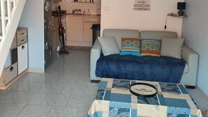 A living room with a sofa, a coffee table, and a kitchen in the background. - Pavillon Pour 4 Personnes au Bord de L'eau (Leucate)