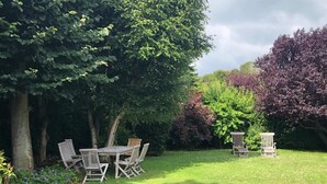 A grassy garden with a wooden table and chairs, surrounded by trees and shrubs. - Villa spacieuse à Dieppe, 3 chambres, 3 salle de bains, jardin fleuri (Dieppe)