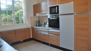 A kitchen with wooden cabinets, a microwave, an oven, and a window with curtains. - Villa spacieuse à Dieppe, 3 chambres, 3 salle de bains, jardin fleuri (Dieppe)