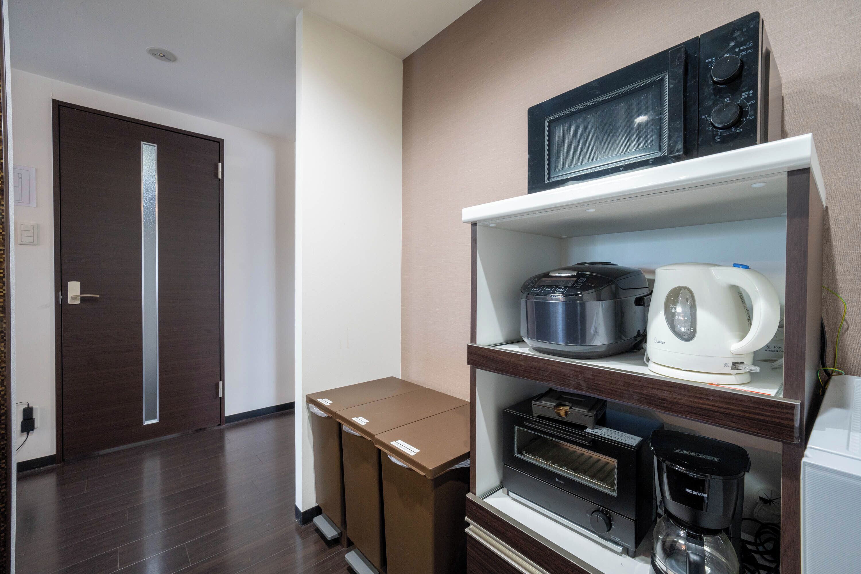 Una kitchenette con microondas, cafetera y horno tostador sobre una repisa de madera.