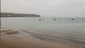 A beach with calm waters, boats, and a cliff in the background. - Bay View (Swanage)