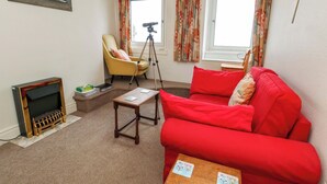 A living room with a red sofa, a small wooden table, a tripod, a yellow armchair, and a framed picture on the wall. - Bay View (Swanage)