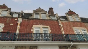 A row of red brick townhouses with white window frames and black wrought iron balconies. - Bay View (Swanage)