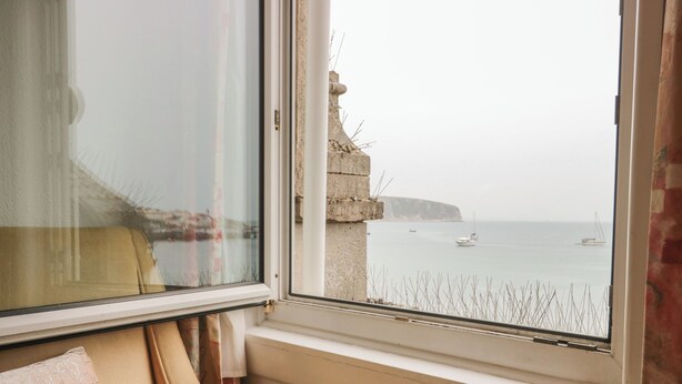 A room with a view of the sea, a chair, and a window sill. - Bay View (Swanage)