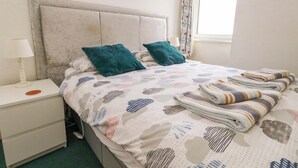 A bedroom with a bed, pillows, a nightstand, a lamp, a painting, and a window. - Bay View (Swanage)