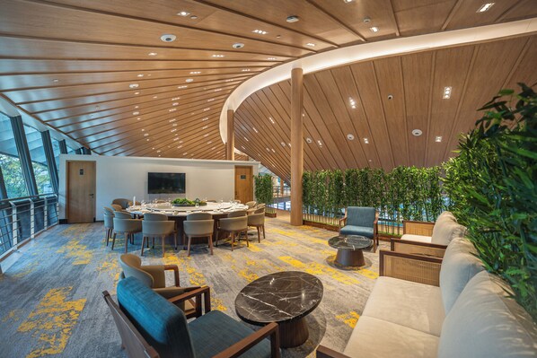 A modern interior with a curved wooden ceiling, a dining area with round tables, and a seating area with sofas and chairs.