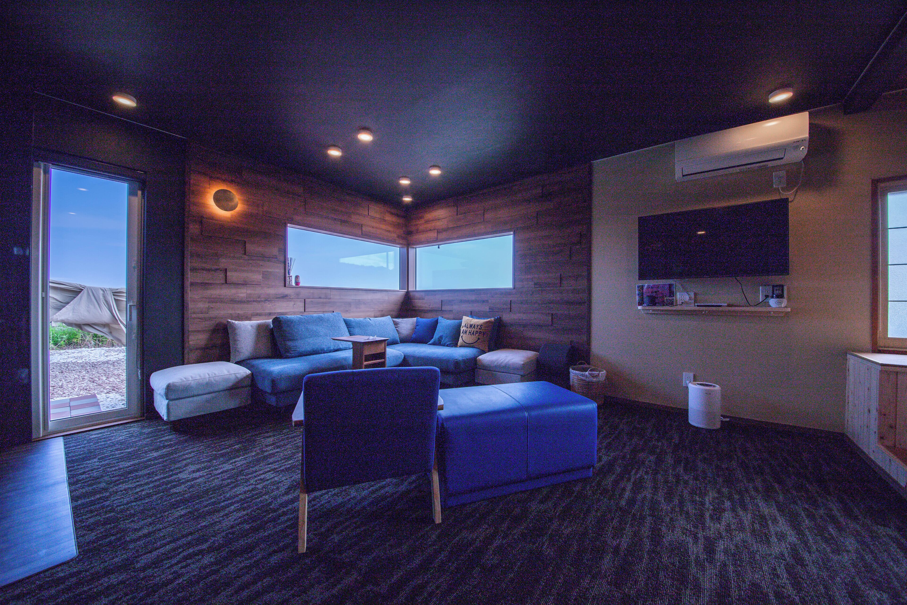 A modern living room with a sectional sofa, ottoman, and a flat-screen TV mounted on the wall.