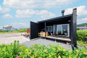 Eine moderne Hütte mit Schiebetür, einer Holzterrasse und einem großen Fenster.