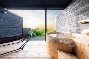 Zona de spa de madera con un jacuzzi, una hamaca y vistas del atardecer.