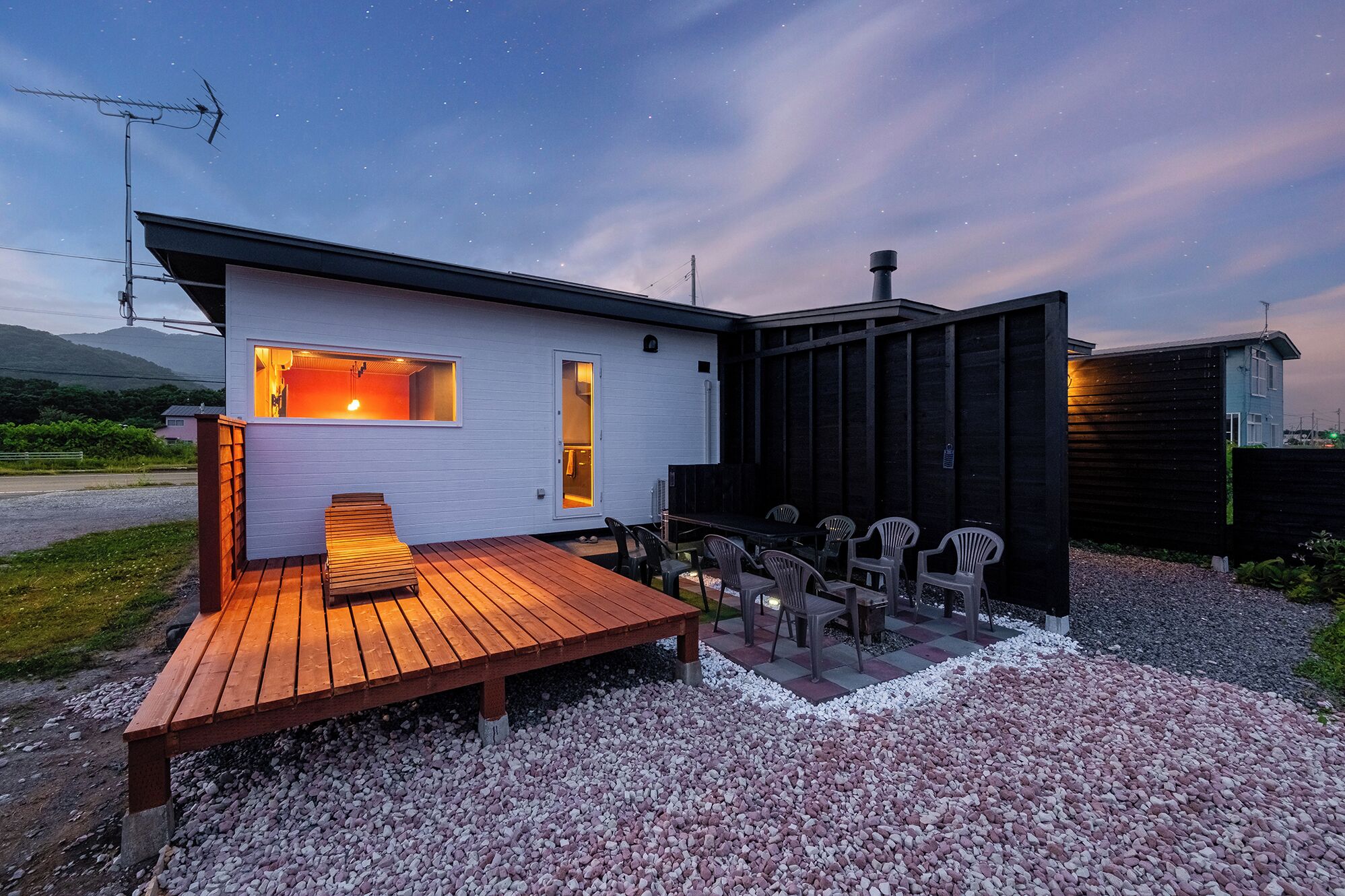 Una casa moderna con terraza de madera, mobiliario exterior y vista al cielo nocturno.